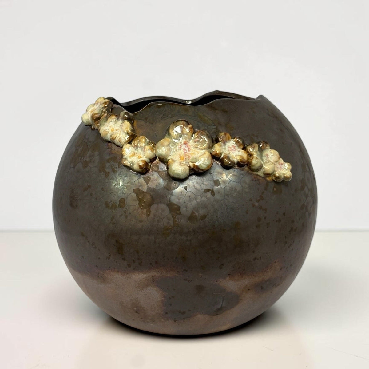 A round ceramic planter or vase with a dark brown and black glazed finish, featuring a raised, textured cream and gold floral border along the rim, set against a plain white background.