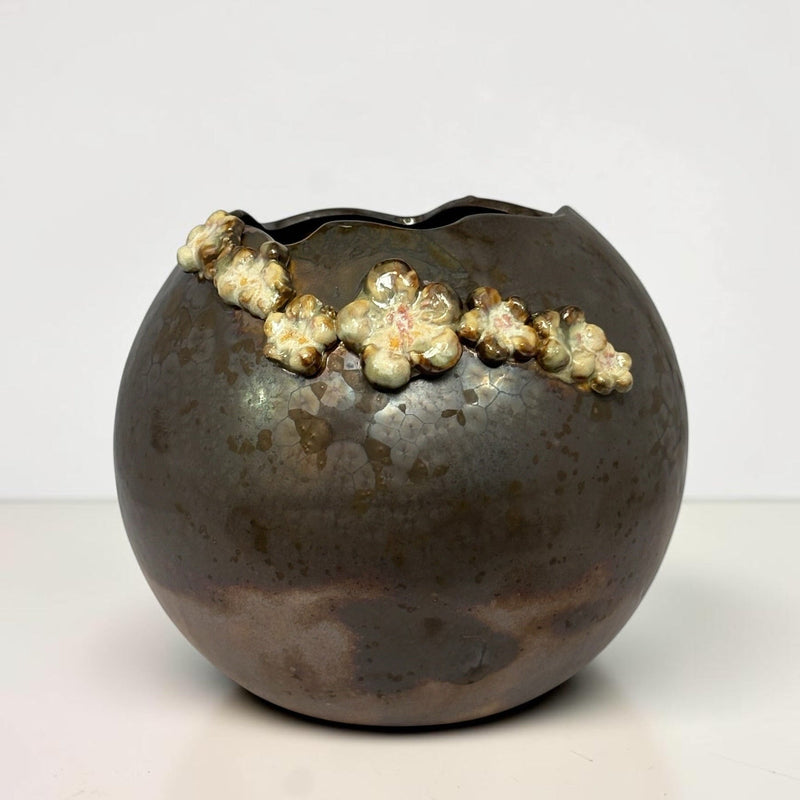 A round ceramic planter or vase with a dark brown and black glazed finish, featuring a raised, textured cream and gold floral border along the rim, set against a plain white background.