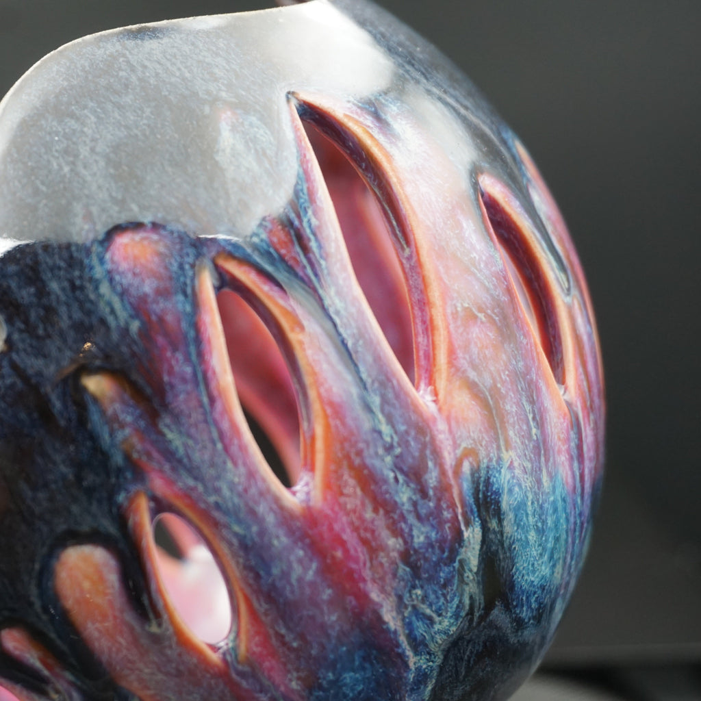 Close-up of a sculptural ceramic vase with organic, organic-looking organic shapes, featuring a glossy finish with marbled swirls of blue, purple, pink, and metallic silver.