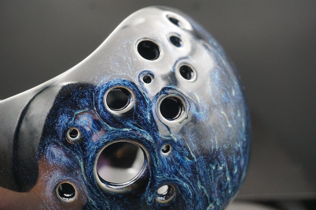 Close-up of a ceramic flute headjoint featuring a marbled blue and silver glaze with multiple circular finger holes.