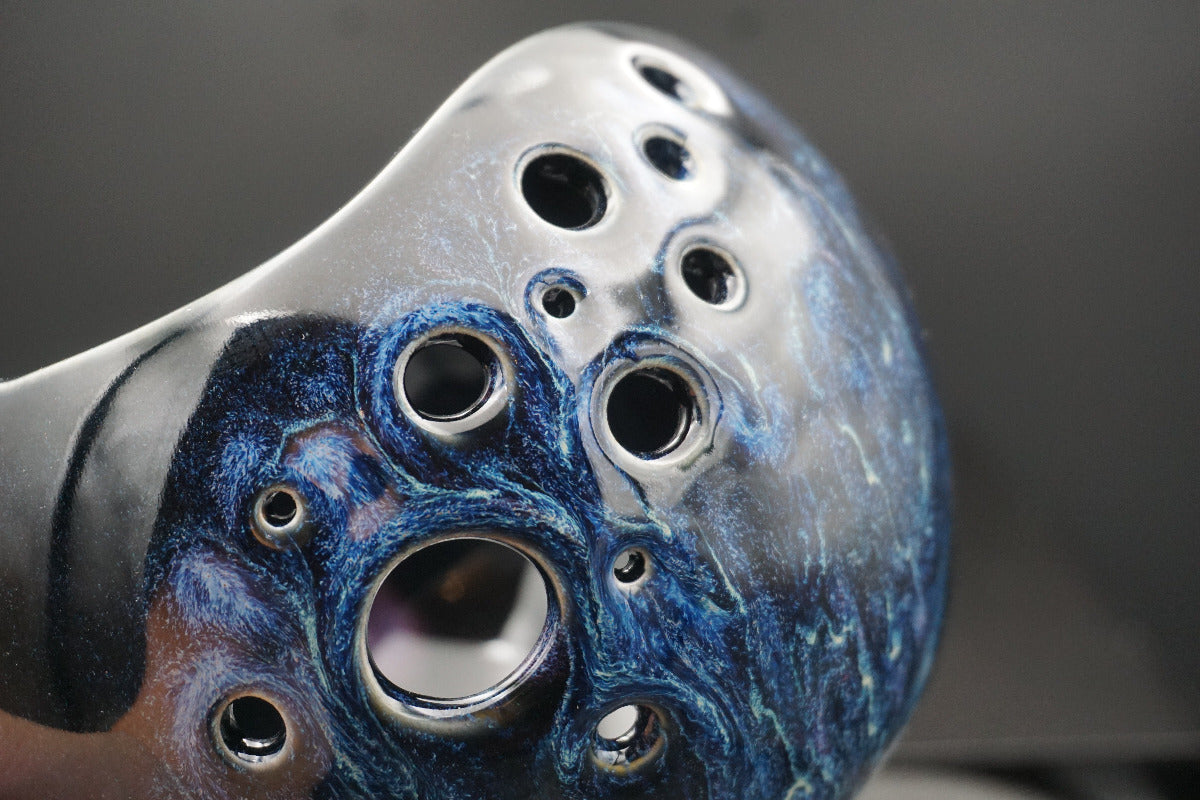 Close-up of a ceramic flute headjoint featuring a marbled blue and silver glaze with multiple circular finger holes.